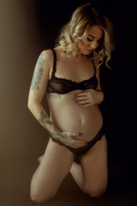 pregnant woman holding her belly in a black bralette and panty for a boudoir shoot