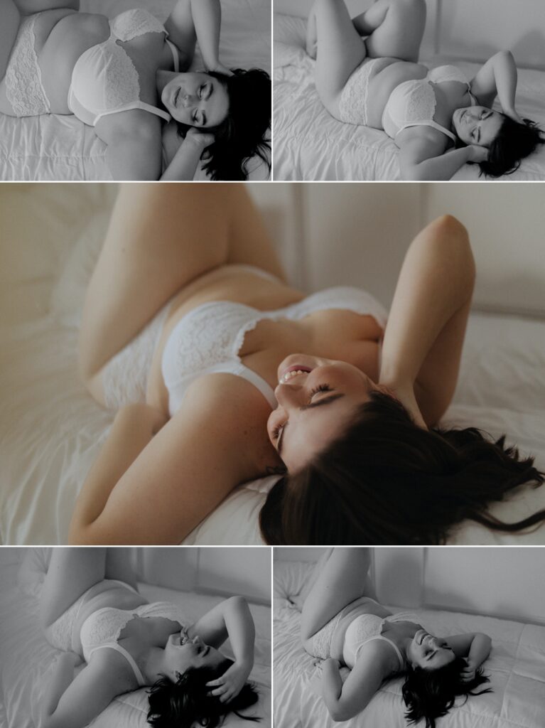 a pretty plus sized woman with dark brown hair lays on a white comforter wearing a white lace bra and panties, runs hands through hair for boudoir photoshoot/photos
