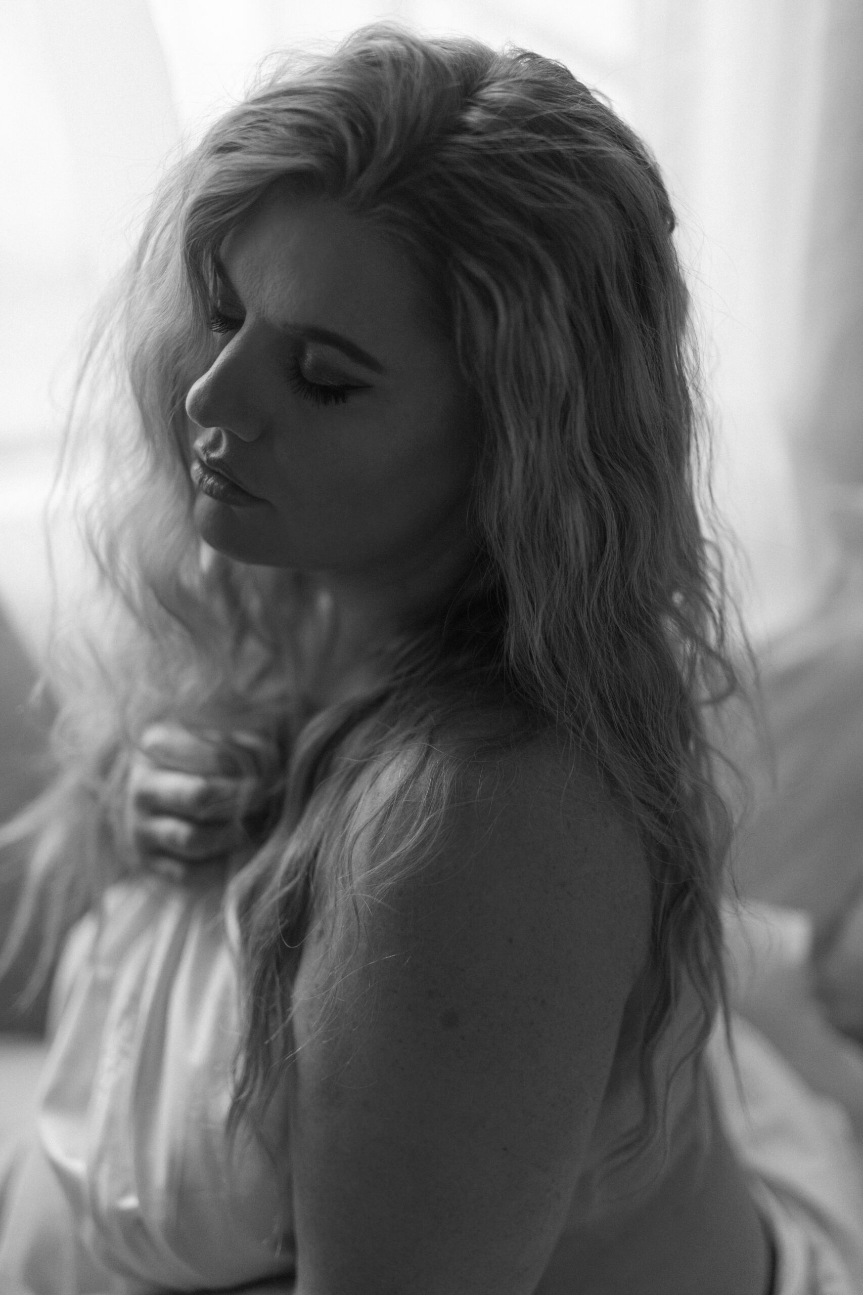 black and white photo of a woman wrapped in a white sheet, looking to the left of frame during a boudoir photography shoot